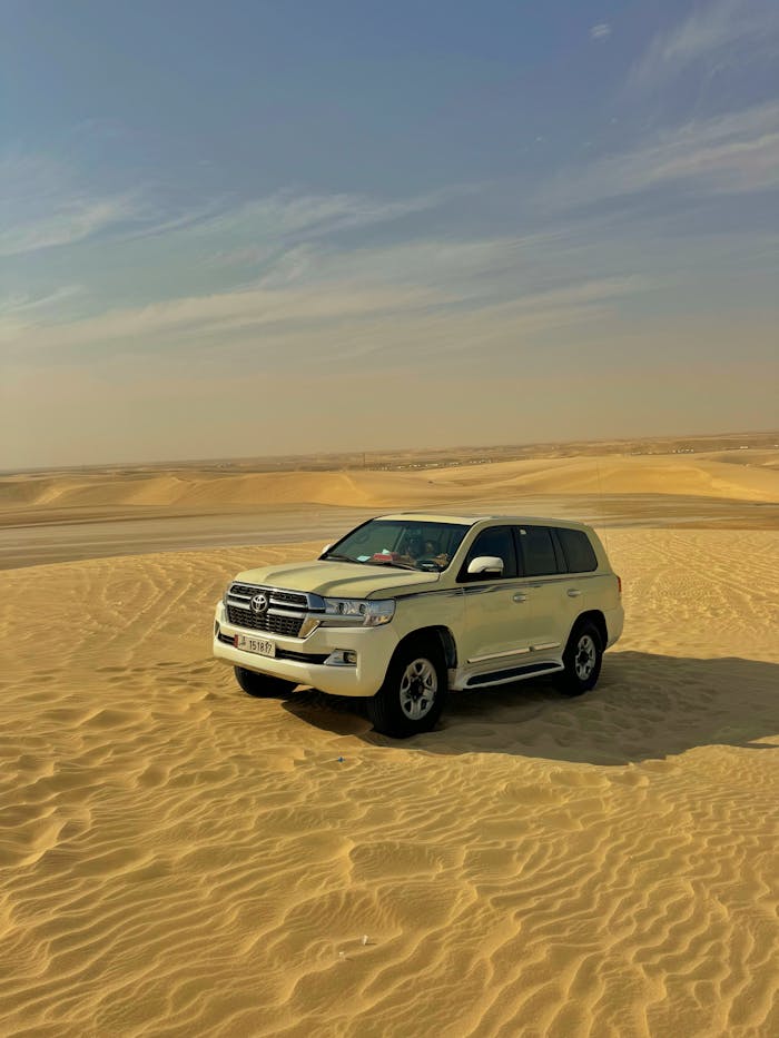 pexels-photo-30698575 White SUV parked on the golden desert dunes under a clear sky in Qatar.