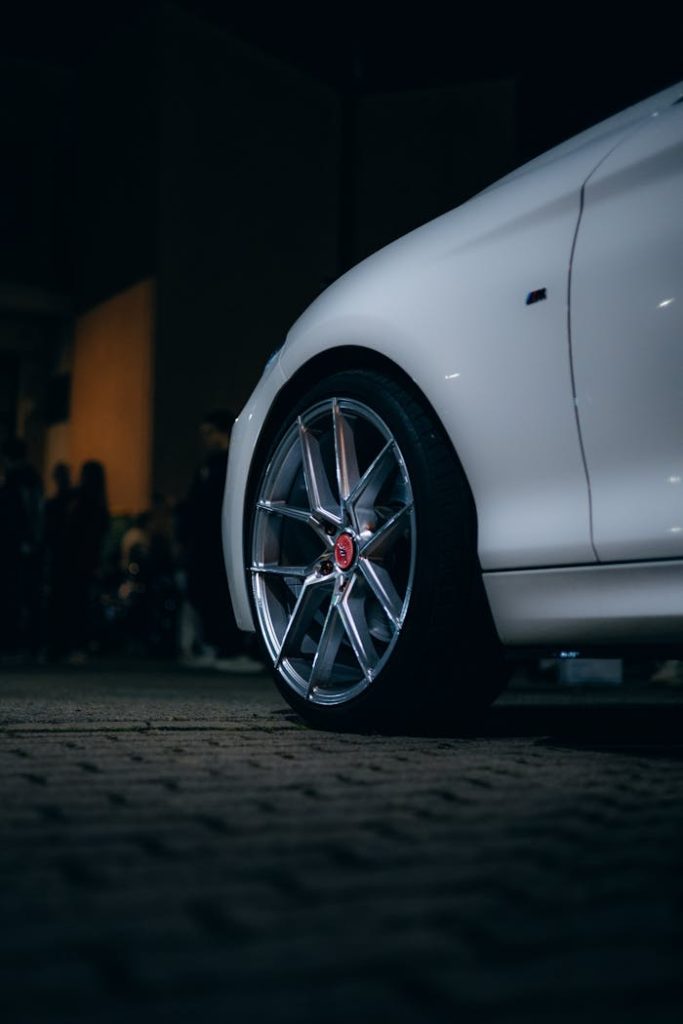 pexels-photo-31727907 Close-up of a white car with alloy wheels parked outdoors at night.